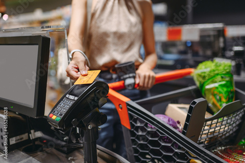 Foto Cropped close up woman hand shopping at supermaket put credit card to wireless modern bank payment terminal process acquire payments near cashier checkout with cart inside store