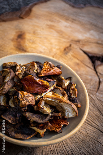 Bright brown dried mushrooms in a white ceramic bowl on wooden background. Rustic indoor design, food closeup. Selective focus on the ingredients, blurred background.