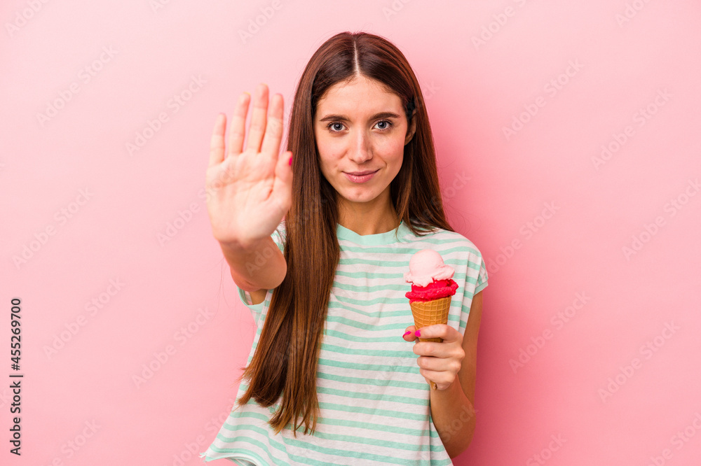 Young caucasian woman holding an ice cream isolated on pink background standing with outstretched hand showing stop sign, preventing you. Young caucasian woman holding an ice cream isolated on pink background standing with outstretched hand showing stop sign, preventing you.