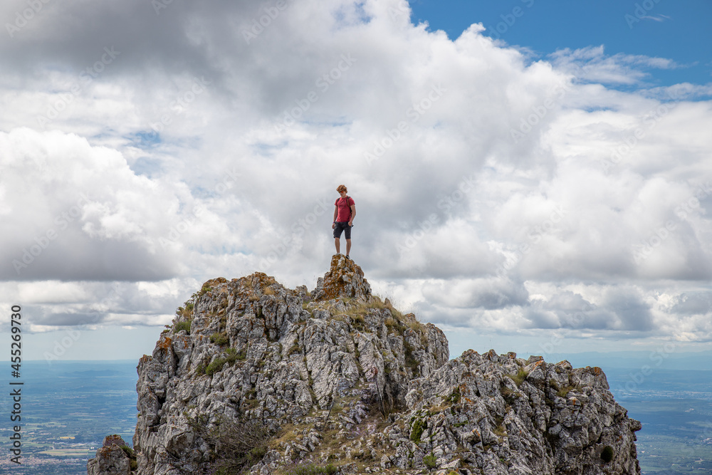 Jeune homme au sommet d'une montagne devant un ciel nuageux, photo évoquant le succès, la victoire, la réussite et le défi