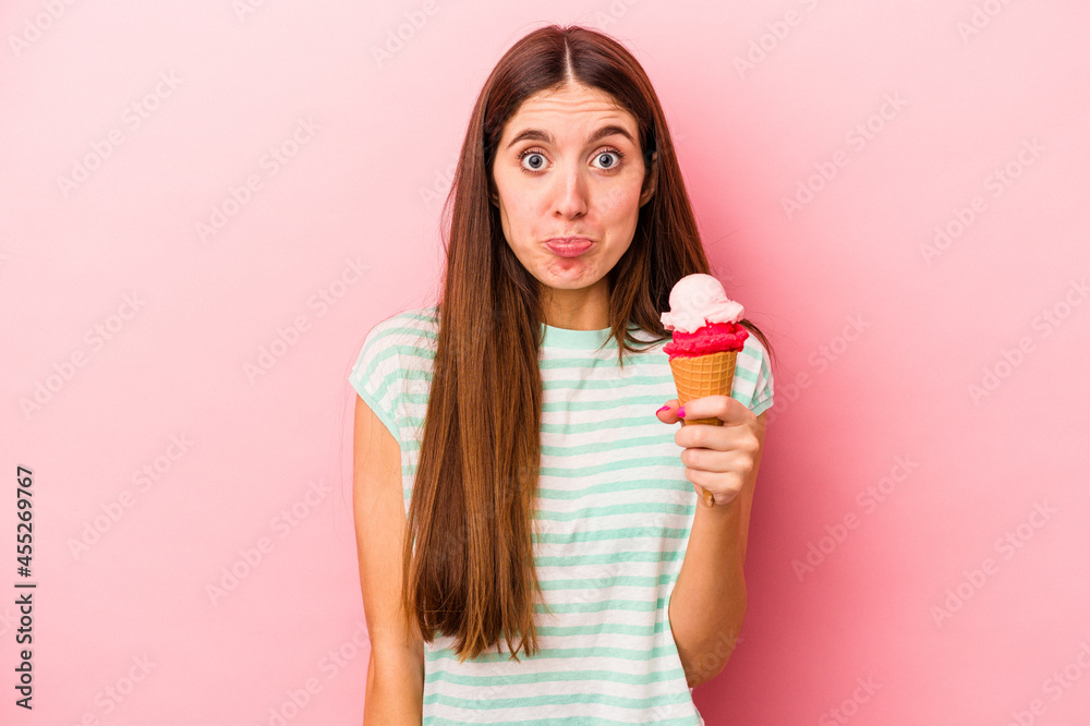 Young caucasian woman holding an ice cream isolated on pink background shrugs shoulders and open eyes confused. Young caucasian woman holding an ice cream isolated on pink background shrugs shoulders and open eyes confused.
