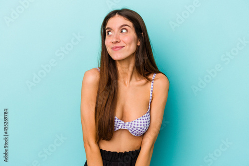 Young caucasian woman wearing bikini isolated on blue background dreaming of achieving goals and purposes