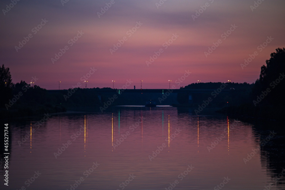 Sunset and its reflection on the water surface of the river. Dark colors and silhouettes of trees on the shore. Copy space