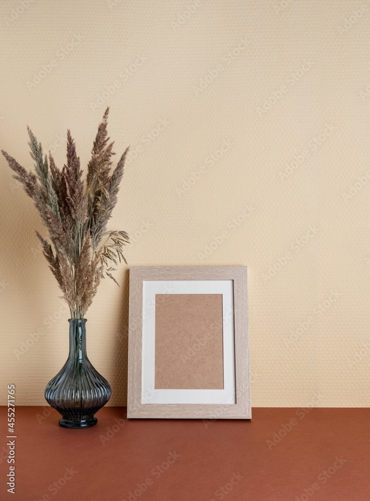 Modern home decor with Pampas grass in vase, mock up beige photo frame, on neutral background. Autumn, fall concept.