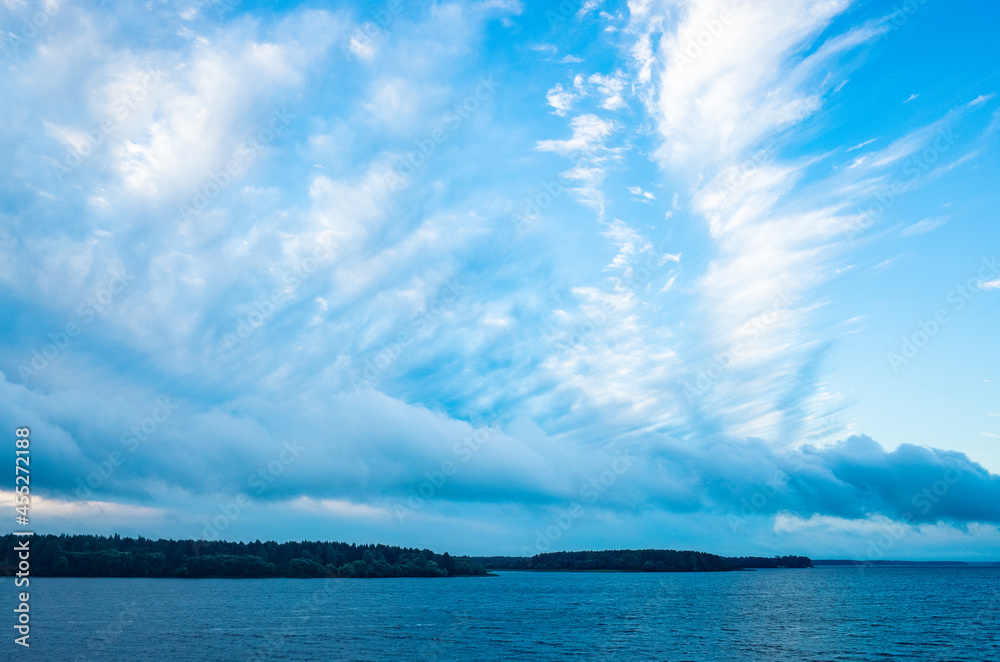 River landscape. Calm water and beautiful blue sky with clouds. Trees grow on the nearest shore. There is copy space