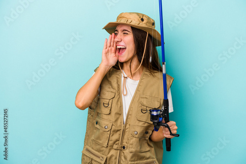 Young caucasian fisherwoman isolated on blue background shouting and holding palm near opened mouth.