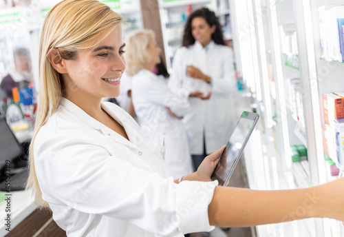 Young female pharmacist working in pharmacy using digital tablet during inventory.