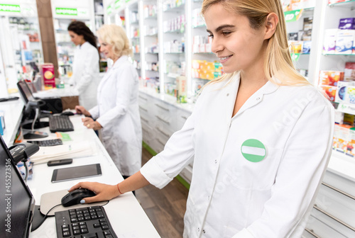 Young female pharmacist working at pharmacy behind the counter.