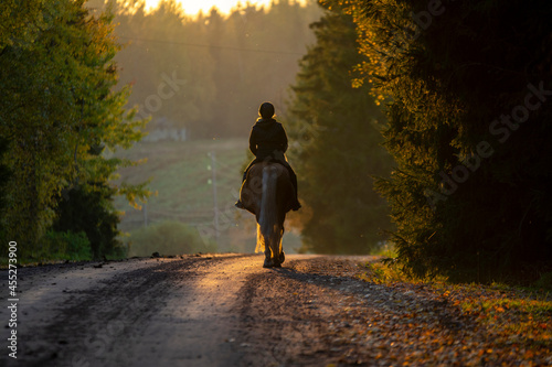 Woman horseback riding on country road at sunset