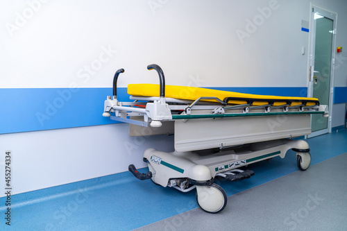Yellow hospital bed on wheels in wide long modern hall in hospital. Horizontal view. Full length photo