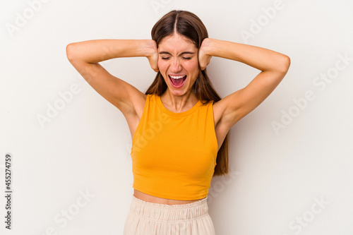 Young caucasian woman isolated on white background covering ears with hands trying not to hear too loud sound.