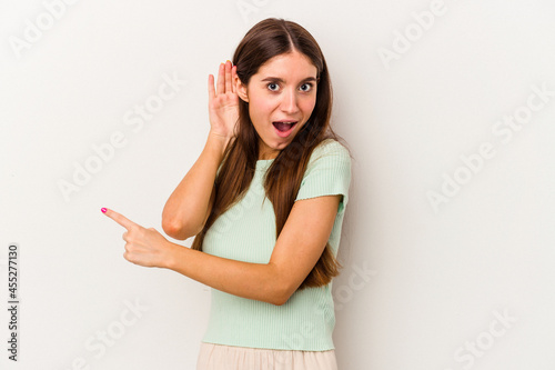 Young caucasian woman isolated on white background trying to listening a gossip.