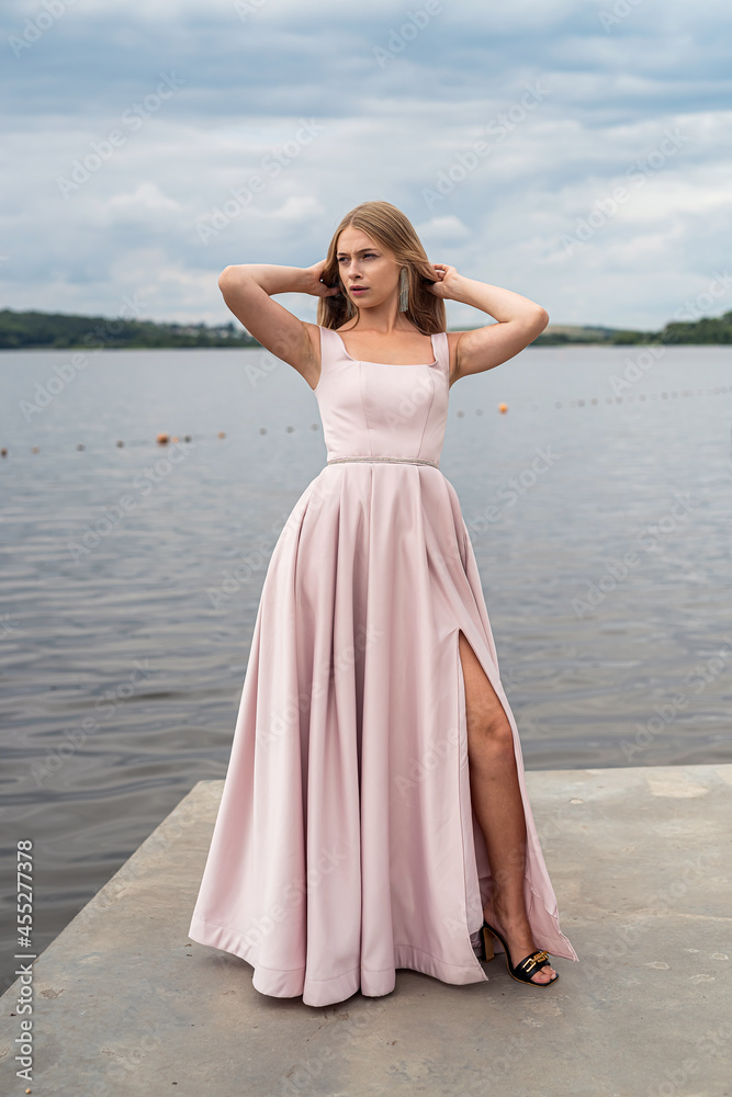 Young woman enjoying summer time posing alone in cute ping dress near lake Young woman enjoying summer time posing alone in cute ping dress near lake