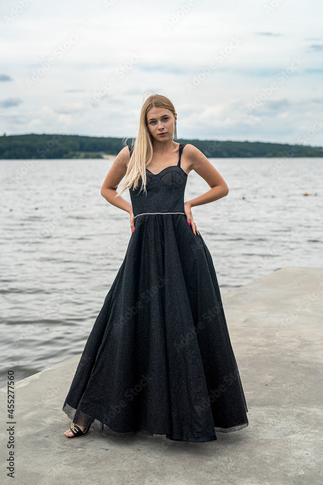 Beautiful young woman in evening long black dress near pond Beautiful young woman in evening long black dress near pond