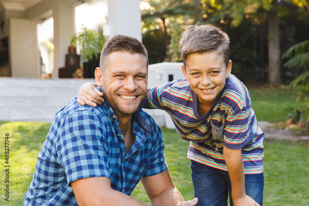 Portrait of smiling caucasian father and son embracing outside house in garden Portrait of smiling caucasian father and son embracing outside house in garden