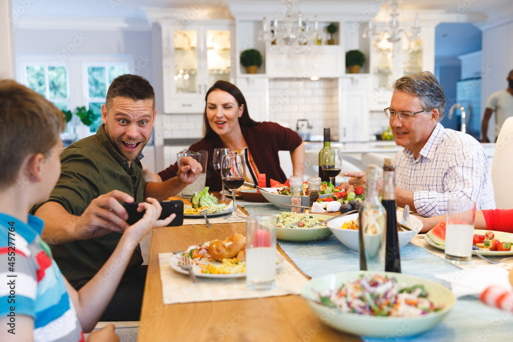 Caucasian grandfather and parents with daughter and son showing phone while having dinner