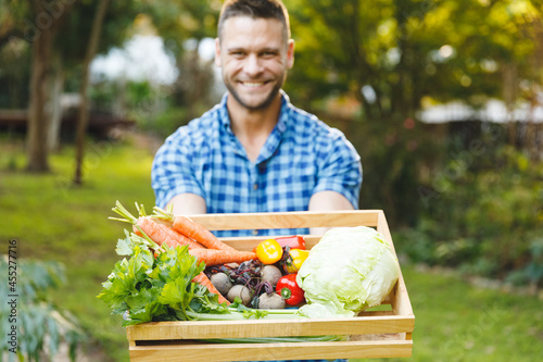 Portrait of smiling caucasian man standing in garden holding box of fresh organic vegetables
