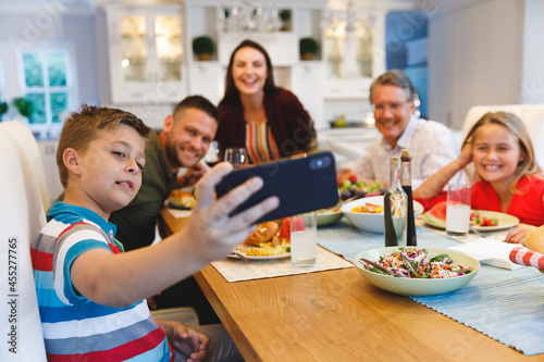 Caucasian grandfather and parents with daughter and son taking selfie while having dinner