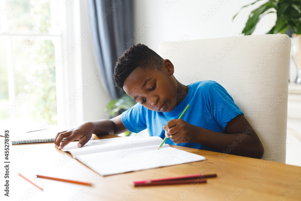 African american boy sitting at table in living room, doing homework African american boy sitting at table in living room, doing homework