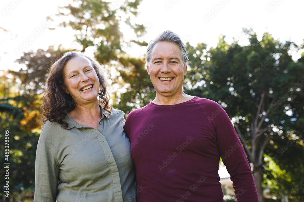 Portrait of happy senior caucasian couple embracing, looking to camera in sunny garden Portrait of happy senior caucasian couple embracing, looking to camera in sunny garden