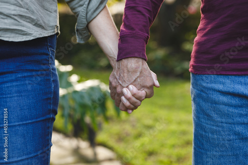 Midsection of senior caucasian couple holding hands walking in garden