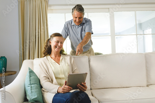 Happy senior caucasian couple in living room, sitting on sofa, using tablet