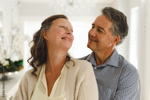 Happy senior caucasian couple in living room, embracing and smiling