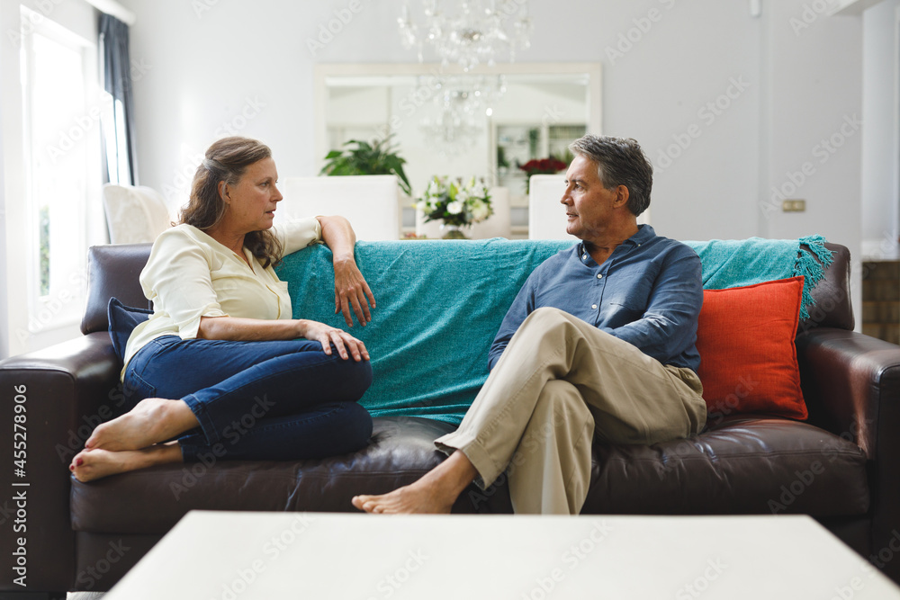 Happy senior caucasian couple in living room sitting on sofa, talking