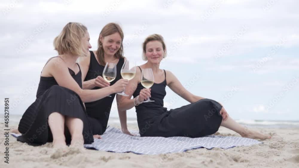Three beautiful women in black dresses drink wine on the beach by the sea from glasses. beautiful stylish video about friendship Three beautiful women in black dresses drink wine on the beach by the sea from glasses. beautiful stylish video about friendship