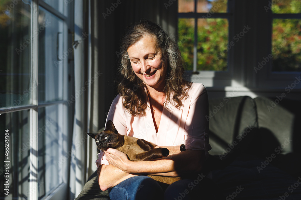 Happy senior caucasian woman in bedroom, holding her pet cat