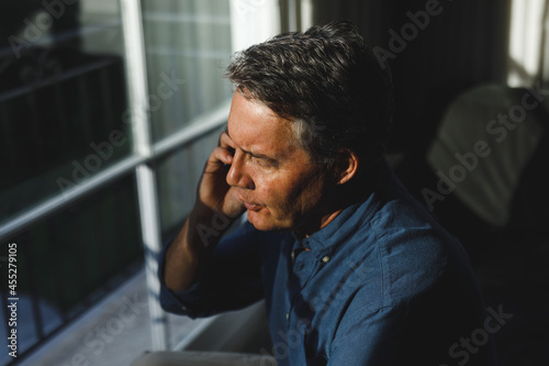 Senior caucasian man in living room sitting on sofa, talking on smartphone