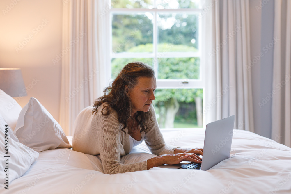 Happy senior caucasian woman in bedroom lying on bed, using laptop Happy senior caucasian woman in bedroom lying on bed, using laptop