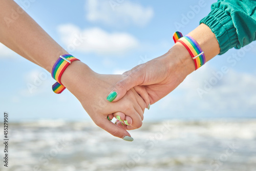 Two caucasian womens holding hands with a rainbow-patterned wristban on their wrists. photo