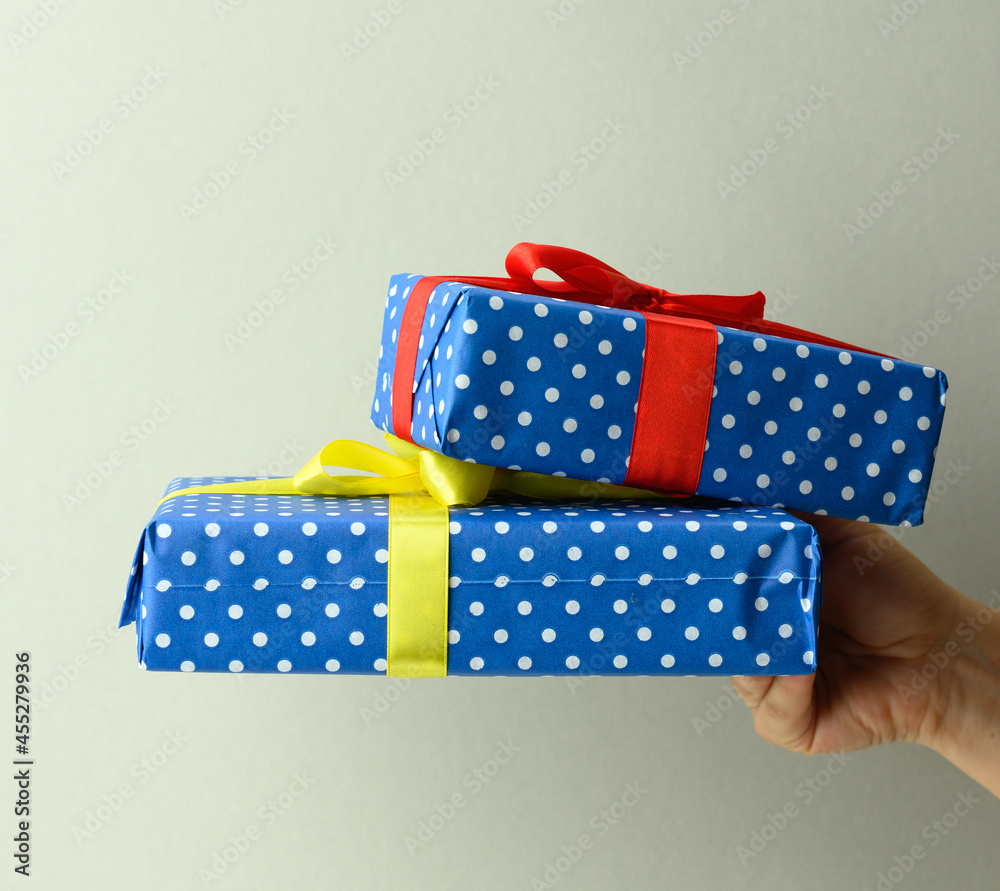 Fototapeta premium female hand holding a stack of gift boxes tied with silk ribbon on a gray background, surprise and win