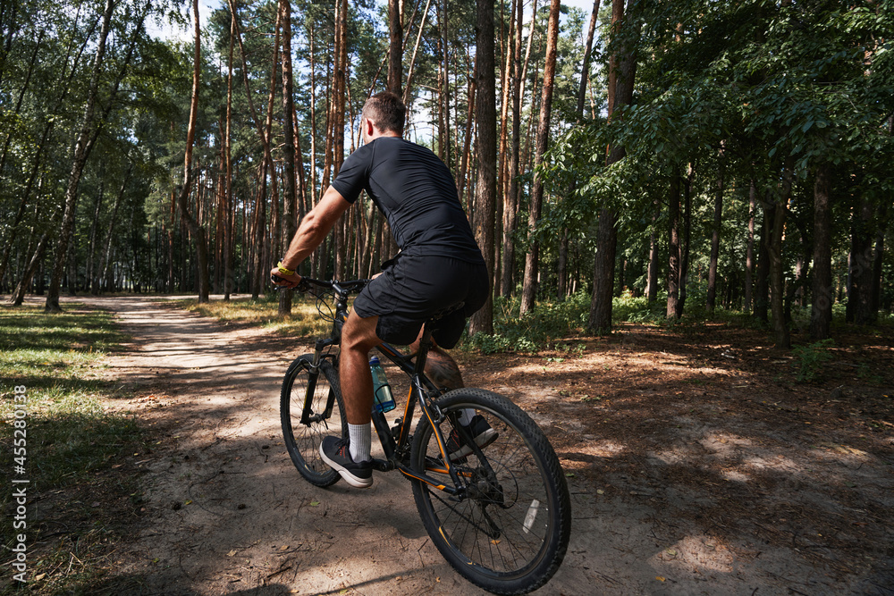 Athletic male riding sporty bike in wood