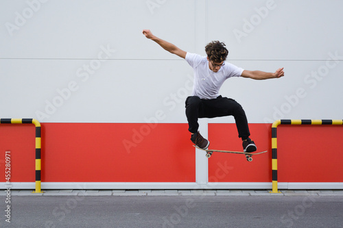 young skater does tricks outdoor. background is white and red wall photo