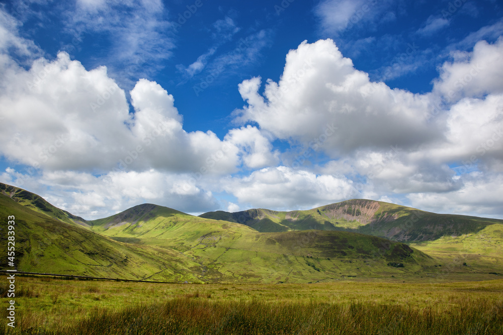 A panoramic view of the mountains of Snowdonia, North Wales. Summer day with blue sky and puffy clouds and the lush green grass of the Welsh countryside.