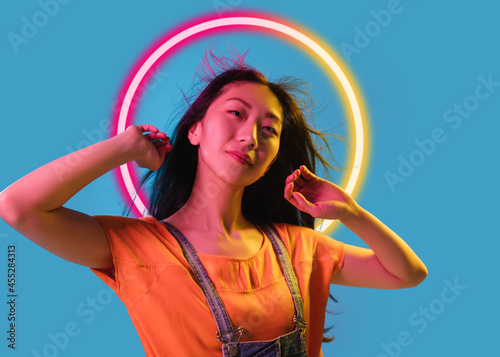Asian woman's portrait isolated on blue studio background in multicolored neon light with geometric luminescent shape cirlce