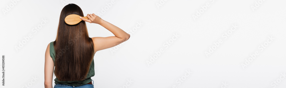 Fototapeta premium back view of young woman brushing hair isolated on grey, banner
