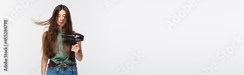 young woman with shiny hair using hair dryer isolated on grey, banner photo