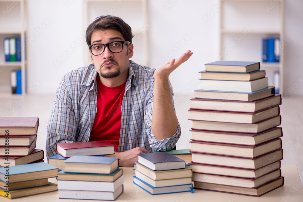Young male student and too many books in the classroom Young male student and too many books in the classroom