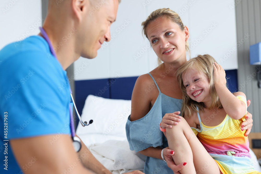 Fototapeta premium Male pediatrician doctor communicates with little girl and mother at medical appointment closeup