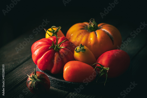 Fresh organic garden tomatoes on rustic table over dark wooden background. Healthy and vegetarian food concept.