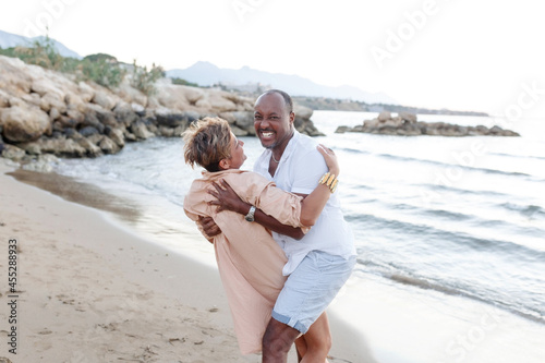 Mixed race smiling couple enjoying on vacation, tourist having fun walking on beachside, diversity and love concept