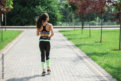 back view of sportive woman in wireless earphones listening music while running in park