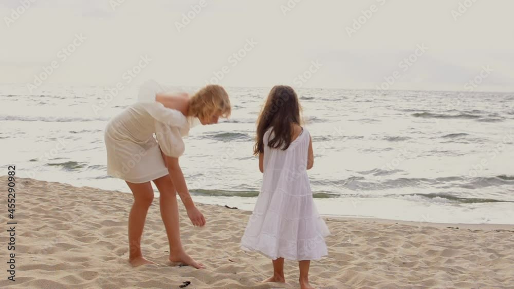 Two pretty girls in white dresses are looking for shells in the sand on the beach. Two pretty girls in white dresses are looking for shells in the sand on the beach.