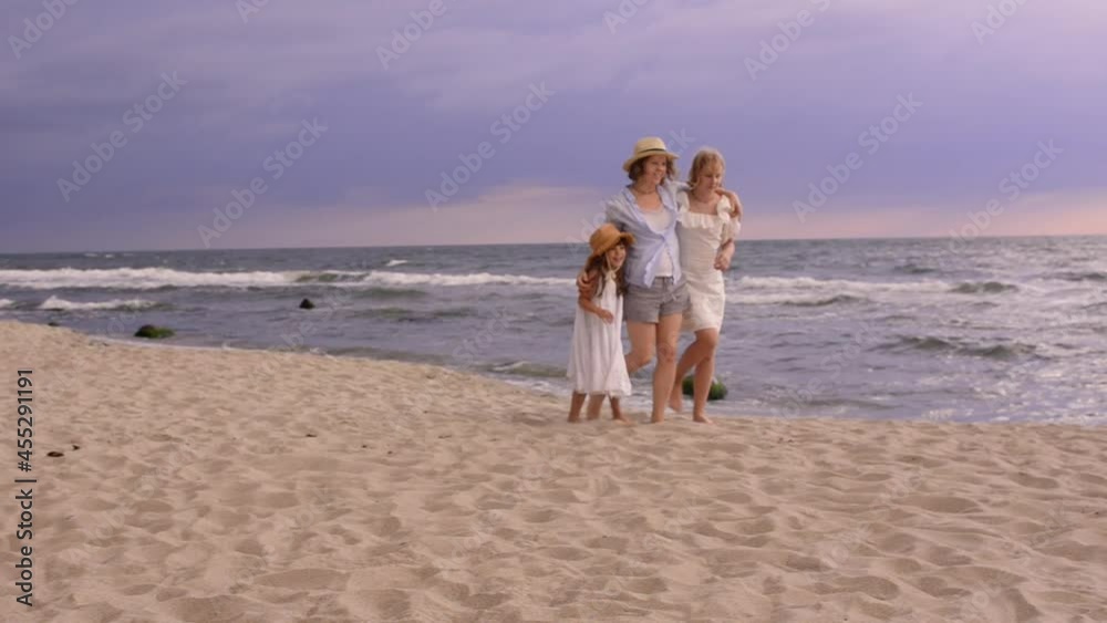 Pretty sisters daughters are walking and hugging on the beach with smiling mother. The family people having fun on summer time. Vacation, travel, love and happiness lifestyle concept. Pretty sisters daughters are walking and hugging on the beach with smiling mother. The family people having fun on summer time. Vacation, travel, love and happiness lifestyle concept.