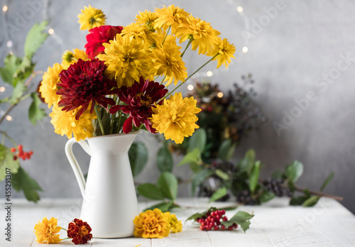 Bouquet of red and yellow flowers in jug on white table. Autumn holiday concept.