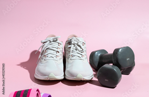 Female sneakers and dumbbells on pink background  for weight workout concept.