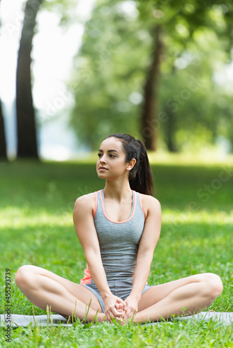 flexible woman in sportswear sitting in lotus pose on yoga mat in park